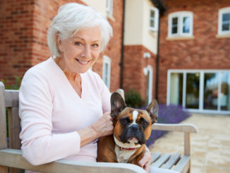 Seniorin mit Hund vor ihrem Wohnsitz